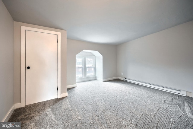 carpeted empty room featuring arched walkways, a baseboard heating unit, and baseboards