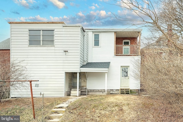 view of front of home with entry steps, a balcony, and a shingled roof