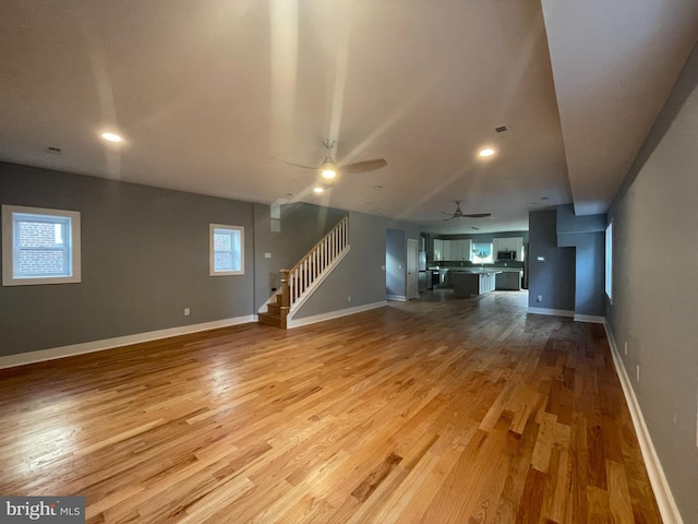 unfurnished living room featuring visible vents, baseboards, ceiling fan, stairway, and light wood-style floors