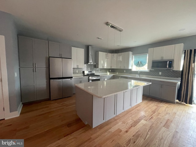 kitchen featuring light wood-style floors, appliances with stainless steel finishes, wall chimney exhaust hood, and a center island