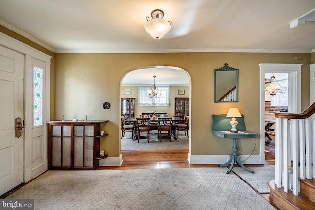 entryway with wood finished floors, arched walkways, an inviting chandelier, crown molding, and baseboards