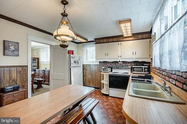 kitchen featuring light countertops, ornamental molding, brick floor, white appliances, and a sink