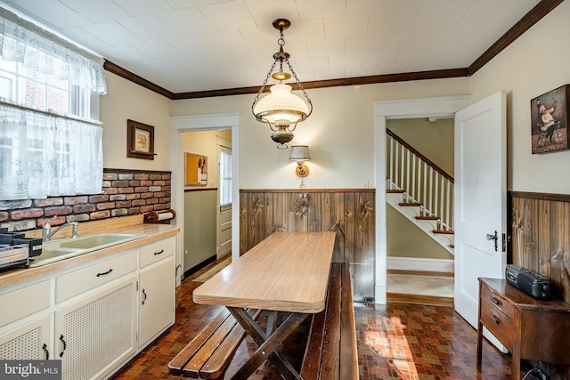 dining area featuring brick floor, stairs, ornamental molding, and wainscoting