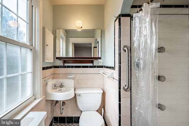 full bath featuring a wainscoted wall, toilet, a sink, tile walls, and tiled shower