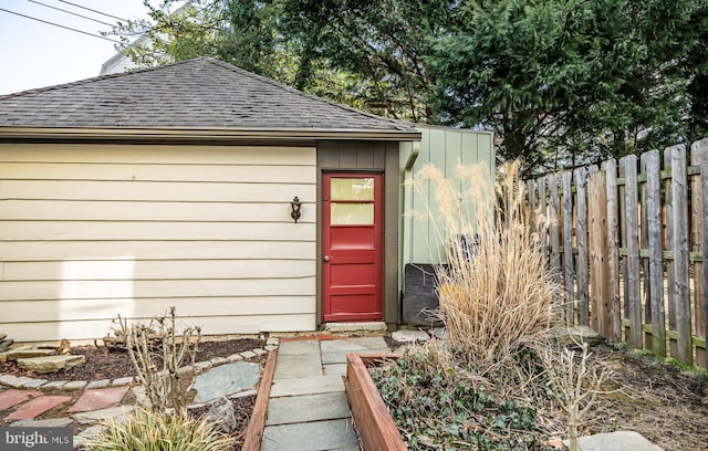 view of exterior entry with roof with shingles and fence