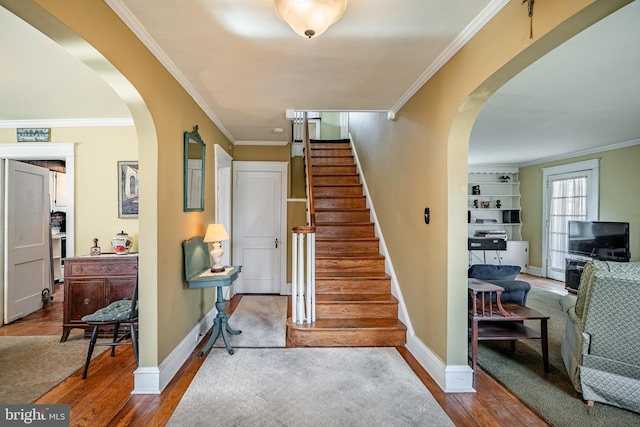 stairs featuring hardwood / wood-style floors, crown molding, baseboards, and arched walkways