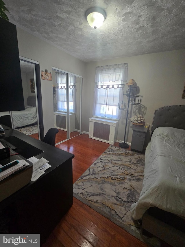 bedroom with baseboards, radiator heating unit, wood finished floors, a textured ceiling, and two closets