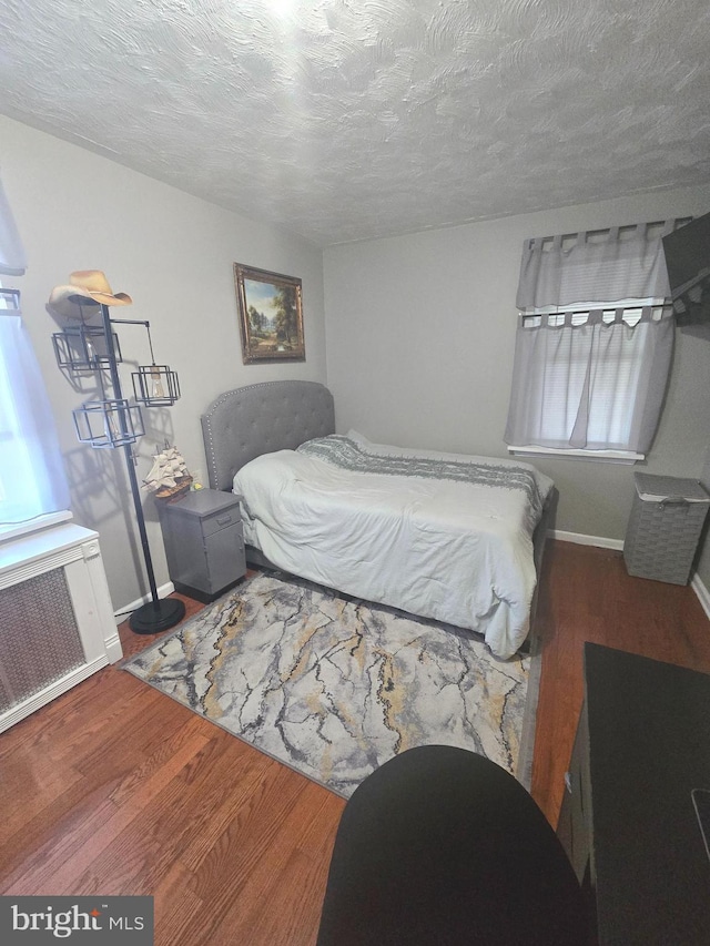 bedroom featuring radiator heating unit, a textured ceiling, baseboards, and wood finished floors