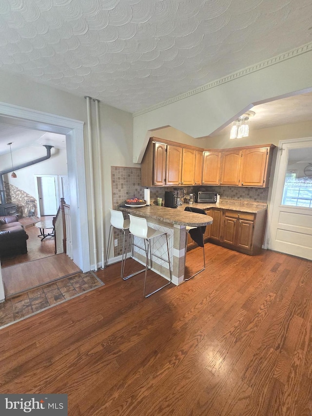 kitchen with a peninsula, a kitchen bar, decorative backsplash, and dark wood-style flooring