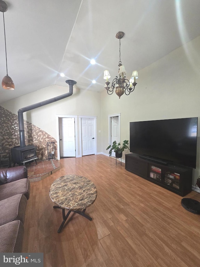 living room with a wood stove, an inviting chandelier, vaulted ceiling, and wood finished floors