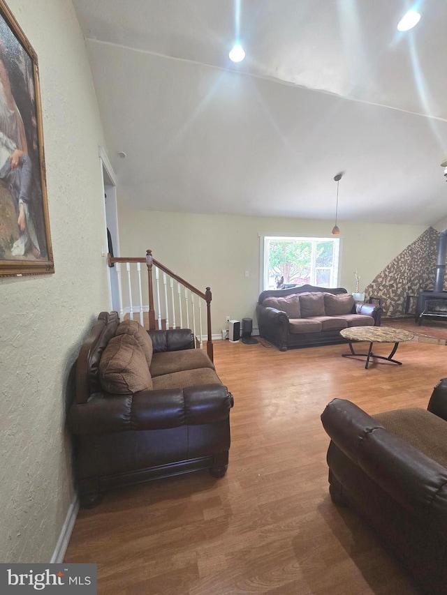 living room featuring baseboards, a textured wall, lofted ceiling, wood finished floors, and a wood stove