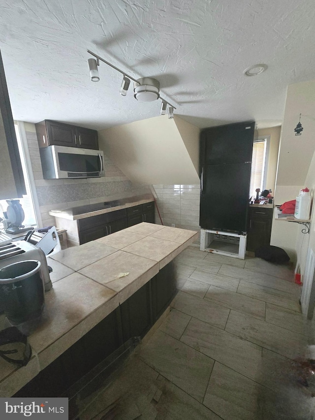 kitchen with tile counters, stainless steel microwave, a textured ceiling, and track lighting