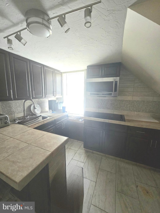 kitchen featuring lofted ceiling, a sink, backsplash, and a textured ceiling