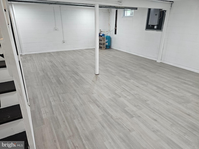 basement featuring wood finished floors, electric panel, and concrete block wall