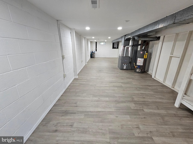 hallway with recessed lighting, gas water heater, concrete block wall, and wood finished floors