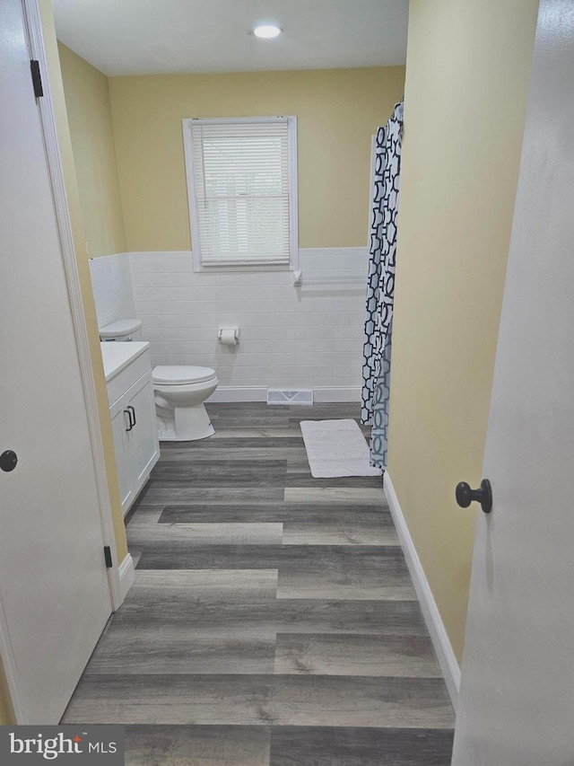 bathroom with a wainscoted wall, tile walls, toilet, vanity, and wood finished floors