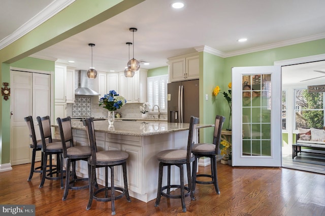 kitchen with dark wood finished floors, a healthy amount of sunlight, wall chimney exhaust hood, and stainless steel refrigerator with ice dispenser