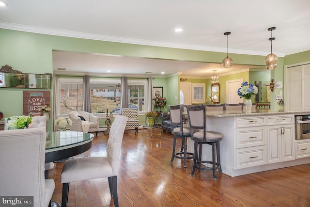 kitchen featuring wood finished floors, a breakfast bar, oven, hanging light fixtures, and white cabinetry