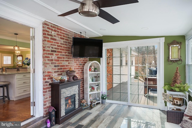 living area featuring wood finished floors, a ceiling fan, lofted ceiling, a fireplace, and crown molding