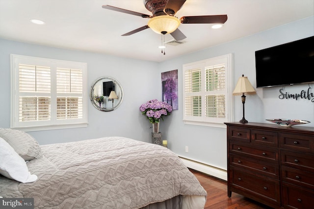 bedroom with visible vents, multiple windows, a baseboard heating unit, and wood finished floors