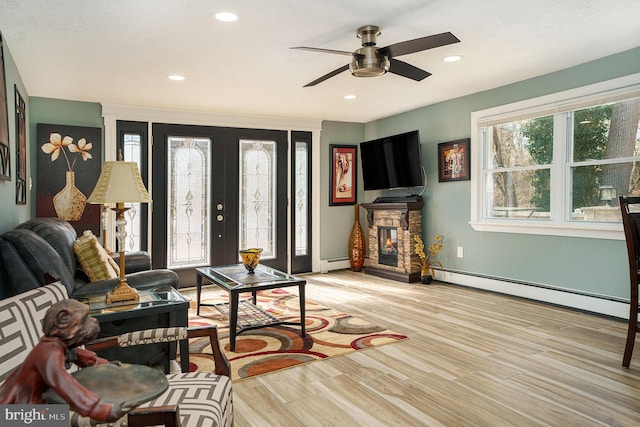 living area with a stone fireplace, recessed lighting, wood finished floors, and a baseboard radiator