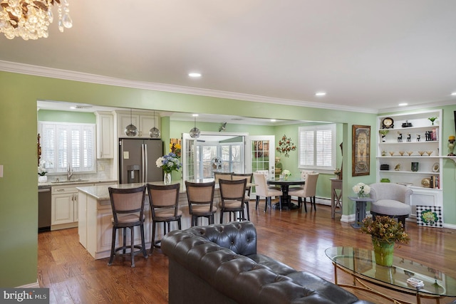 living area with ornamental molding, wood finished floors, recessed lighting, an inviting chandelier, and baseboards