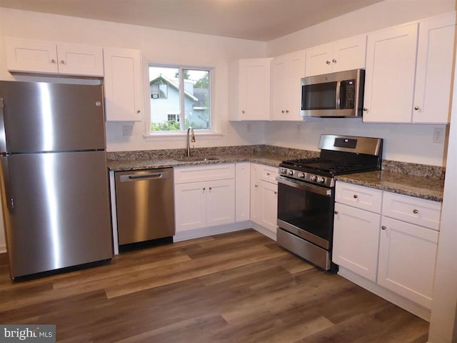 kitchen featuring dark wood-style floors, stainless steel appliances, white cabinetry, a sink, and dark stone counters