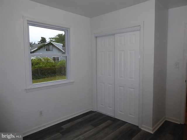 unfurnished bedroom with a closet, dark wood finished floors, and baseboards