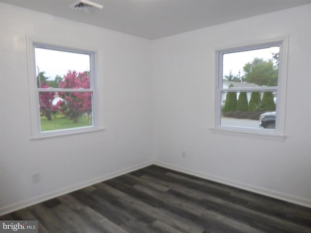 empty room featuring a healthy amount of sunlight, baseboards, visible vents, and dark wood finished floors