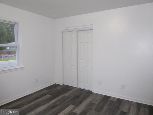 unfurnished bedroom with dark wood-style floors, baseboards, and a closet