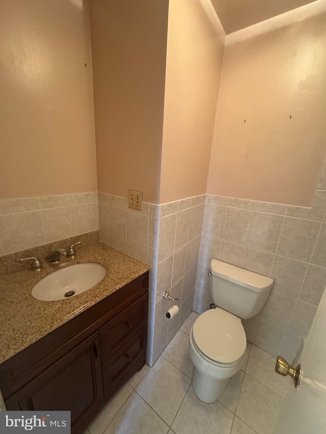 bathroom with toilet, vanity, wainscoting, tile patterned floors, and tile walls