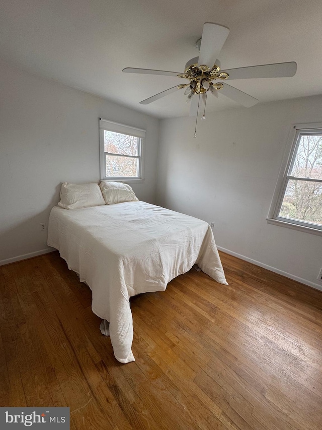 bedroom featuring baseboards, multiple windows, wood finished floors, and a ceiling fan