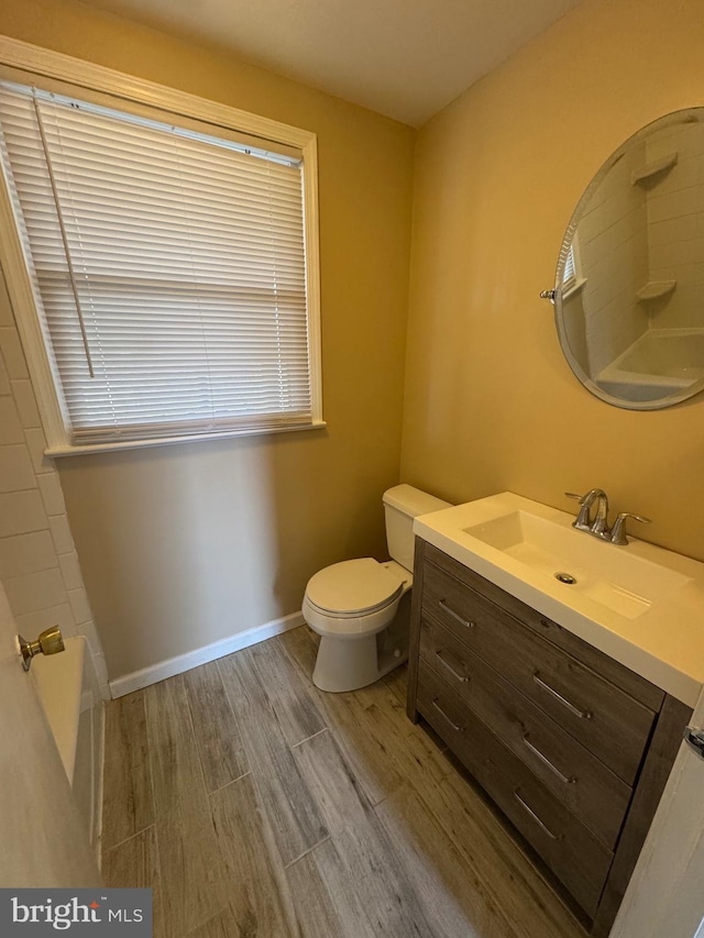 full bath featuring toilet, vanity, baseboards, and wood finished floors