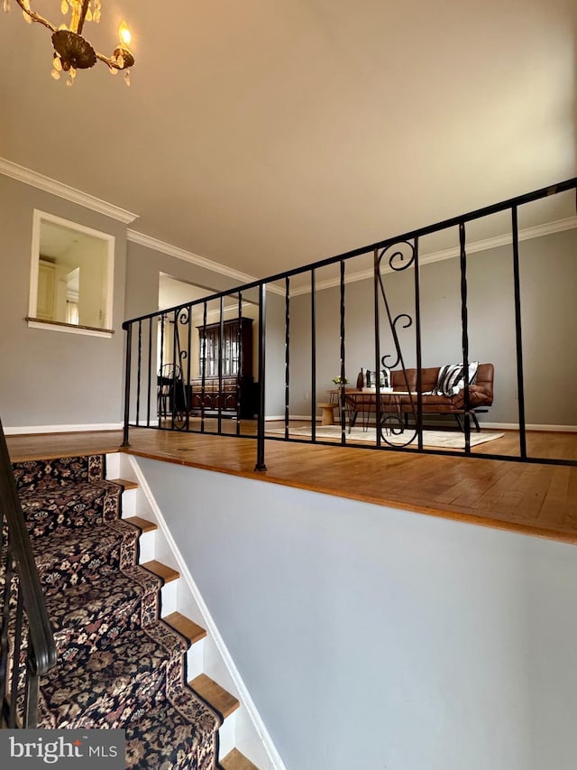 staircase featuring a notable chandelier, crown molding, baseboards, and wood finished floors