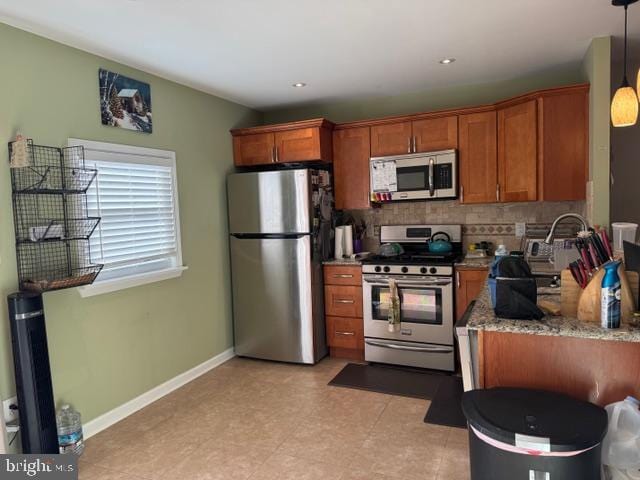 kitchen with baseboards, brown cabinets, hanging light fixtures, appliances with stainless steel finishes, and tasteful backsplash