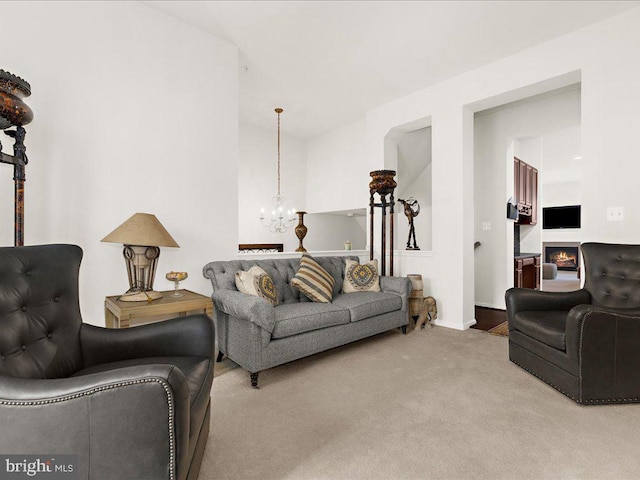 living area featuring an inviting chandelier, baseboards, carpet floors, and a lit fireplace