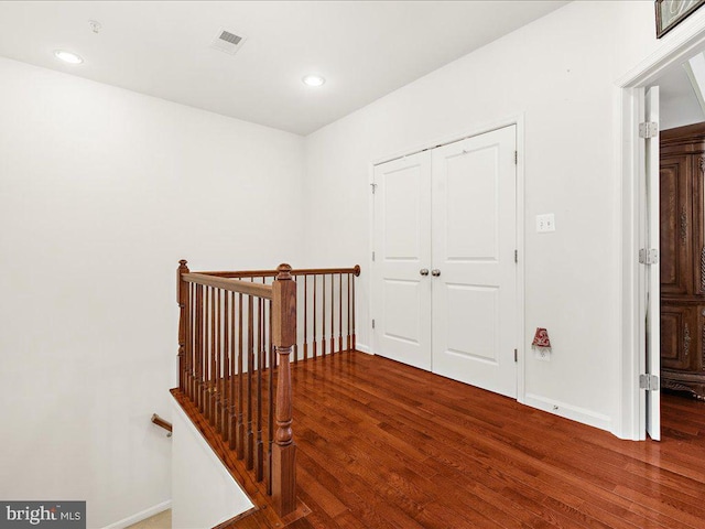 corridor with an upstairs landing, visible vents, baseboards, and wood finished floors