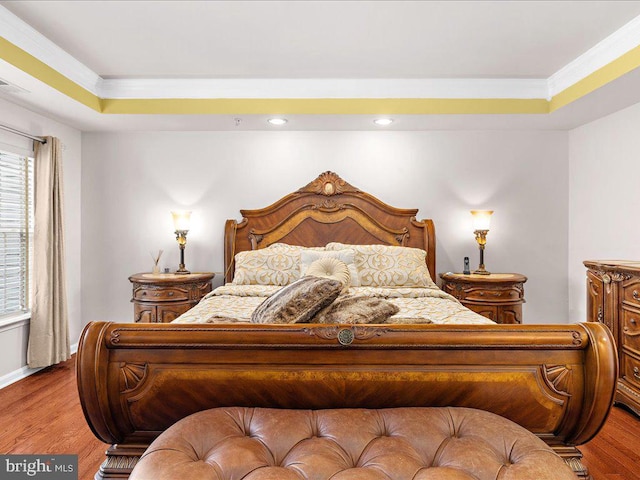 bedroom with a raised ceiling, crown molding, wood finished floors, and baseboards