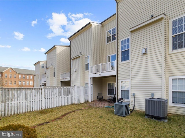 rear view of property featuring fence, a lawn, and central AC