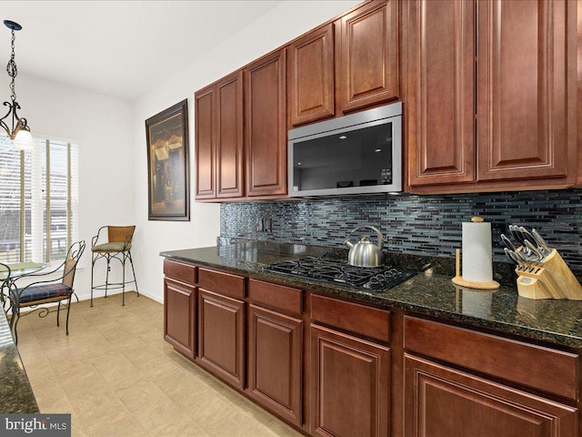 kitchen featuring stainless steel microwave, backsplash, pendant lighting, dark stone counters, and black gas stovetop