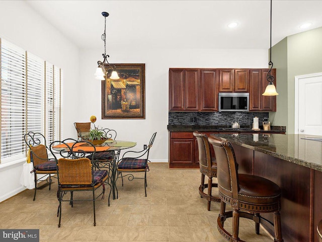 kitchen featuring a breakfast bar, stainless steel microwave, backsplash, baseboards, and hanging light fixtures