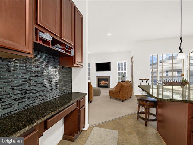 kitchen featuring a breakfast bar area, a lit fireplace, light carpet, open floor plan, and backsplash