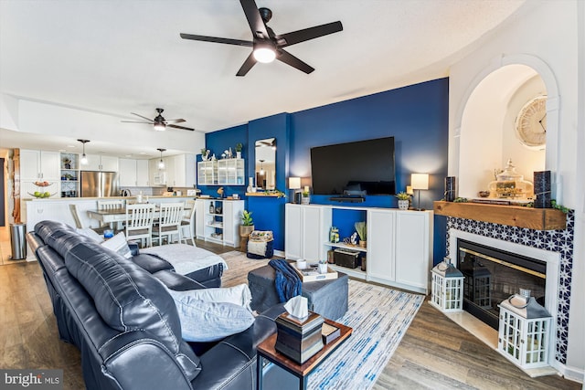 living area featuring a fireplace, a ceiling fan, and light wood finished floors