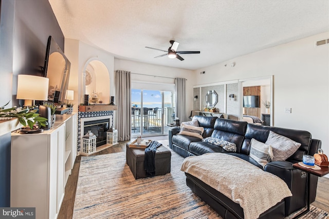 living room featuring a tile fireplace, a textured ceiling, ceiling fan, and wood finished floors