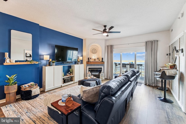 living area featuring baseboards, a tiled fireplace, wood finished floors, a textured ceiling, and a ceiling fan