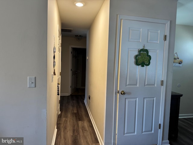 hallway with dark wood-type flooring, visible vents, and baseboards