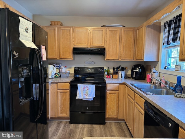 kitchen with a sink, light countertops, ventilation hood, black appliances, and light wood finished floors