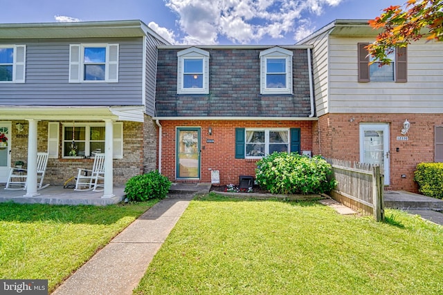 view of property with covered porch, brick siding, fence, mansard roof, and a front yard