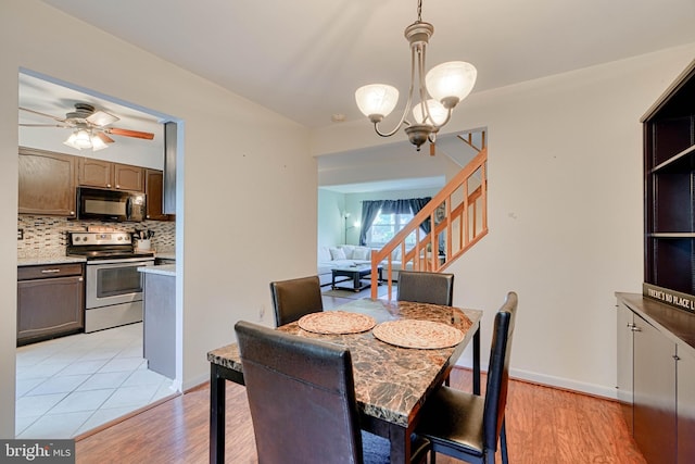 dining space with light wood-type flooring, stairway, and ceiling fan with notable chandelier