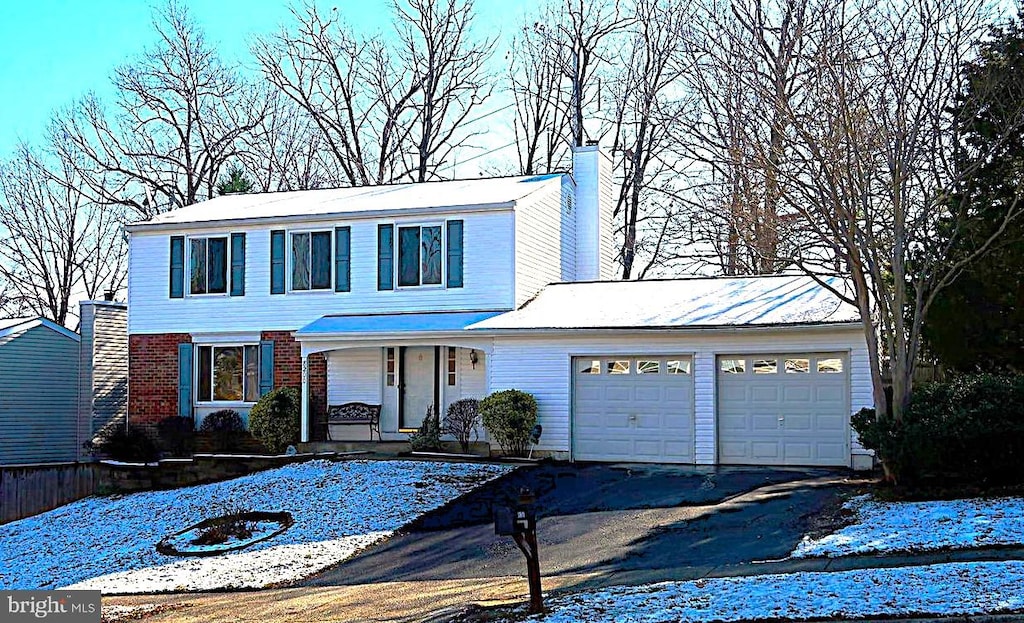 traditional-style house featuring aphalt driveway, brick siding, a chimney, a porch, and an attached garage